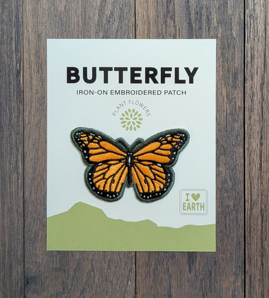 Monarch butterfly iron-on embroidered patch applied to denim fabric, showing vibrant orange and black wings with green border detail.